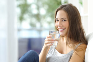Mujer feliz tomando agua mujer sentada en un sofá mirando a la cámara con un vaso de agua